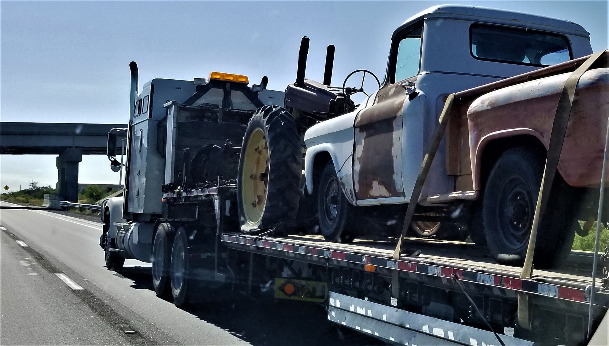 Old model truck and tractor on a flatbed truck being transported