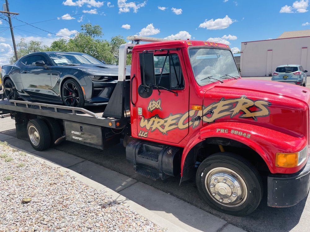 ABQ Wreckers red tow truck with a car on the back being transported.